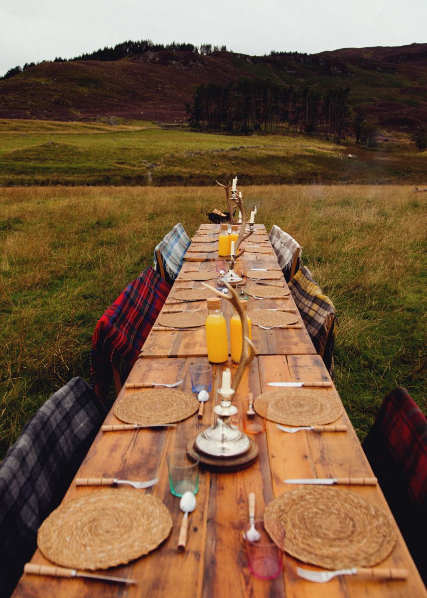 A table in a field set with cutlery, orange juice, and tartan blankets