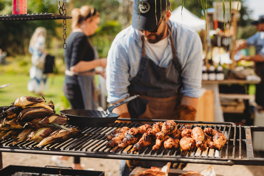 A chef working behind a grill laden with grilled chicken on a sunny day
