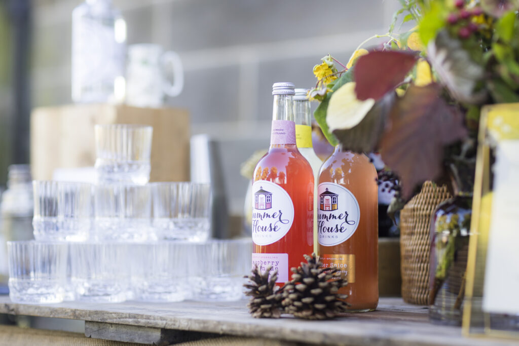 fruit juice in bottles, pine cones, flowers, and a pile of ornate glasses on a wooden palette