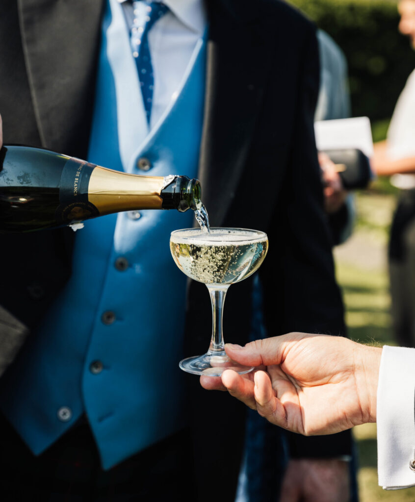 a man pouring champagne into an old fashioned champagne glass held by someone in a shirt