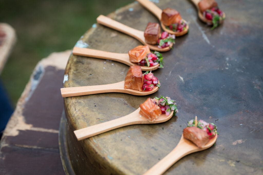 Small spoons of fish, herbs, and pomegranate in a circle on a tin as a wedding catering canapé.