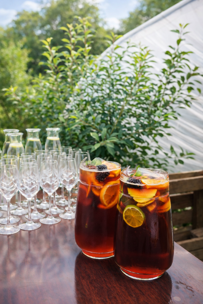 two pitchers of Pimm's with fresh fruit and glasses on a table outside