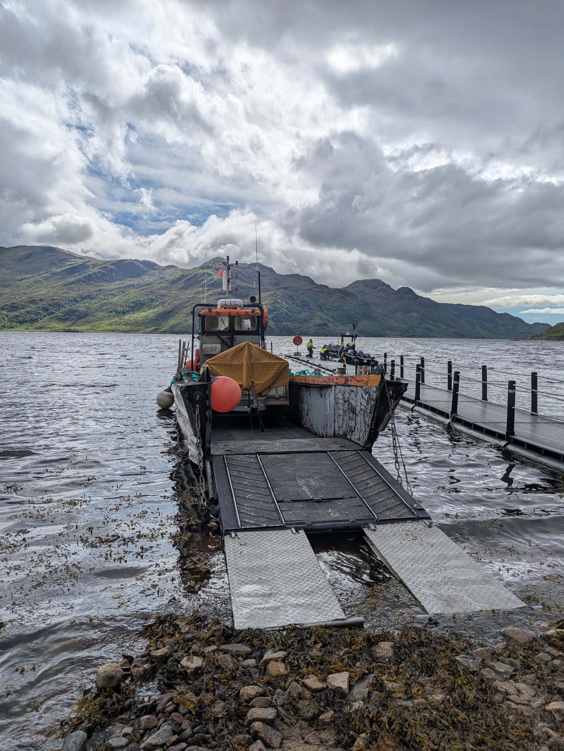 A small boat set against rugged hills and beach carrying a trailer, ready for off-grid marquee events catering logistics