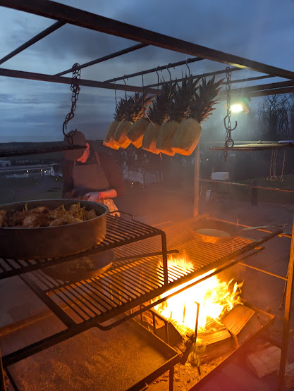 pineapples hanging above a roaring fire in a metal grill barbecue