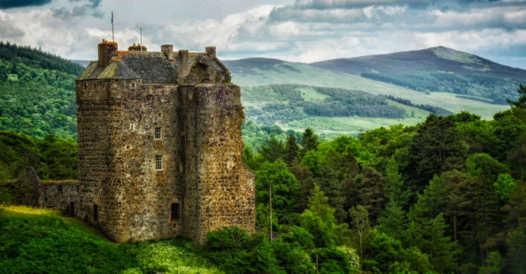 A tall stone castle looks over woody hills